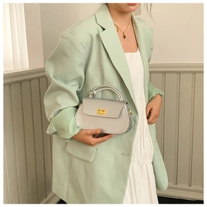 Silver-grey handbag with gold square twist lock and cylindrical handle held by a model