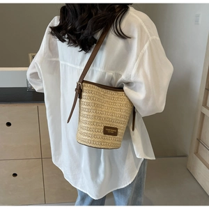 Detailed close-up of woven straw bucket bag with premium brown leather trim and logo