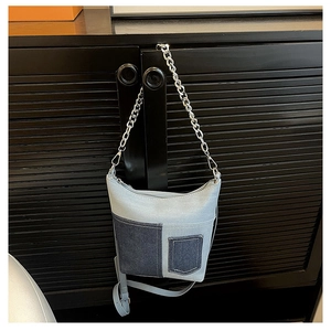 Detail of color-block denim bucket bag featuring silver chain and adjustable strap