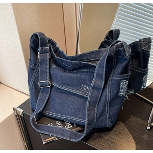 Dettaglio macro della borsa in denim blu scuro con cuciture a contrasto e bordi sfrangiati