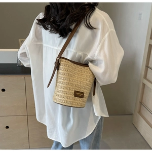 Detailed back view of a woven straw bucket bag with brown leather straps and adjustable buckle