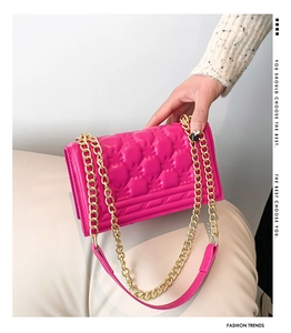 Detail view of rose red quilted crossbody bag with elegant gold chain shoulder strap