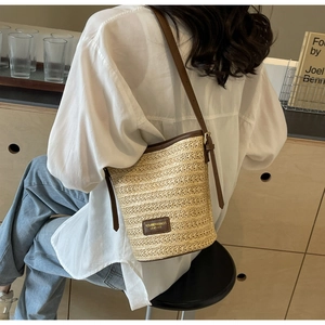 Detail of hand-woven straw bucket bag with dark brown leather trim and adjustable strap