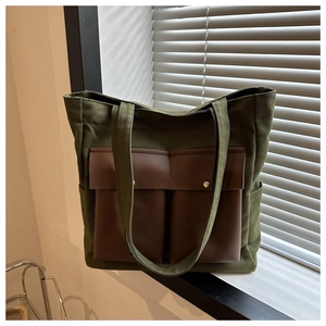 Detail of dark green canvas tote bag featuring double brown leather front pockets