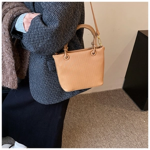 Detail of a brown pleated bucket bag with fine vertical texture and golden metal buckle