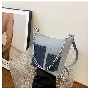 Close-up of light blue denim bucket bag featuring contrast dark pockets and silver chain strap