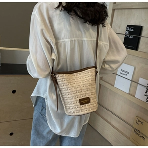 Detail of woven straw bucket bag with dark brown leather straps and brand logo patch