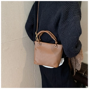 Close-up of brown pleated bucket bag with braided handle and slim shoulder strap detail