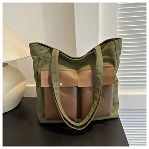 Detail of canvas tote bag showing olive green fabric and brown leather-style front pockets