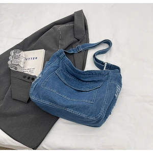 Dettaglio della borsa a tracolla in denim blu con bordi sfrangiati e fibbia in metallo