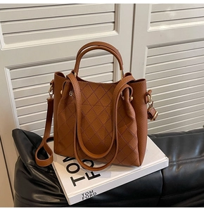 Close-up of brown quilted bucket bag with golden hardware on a decorative book