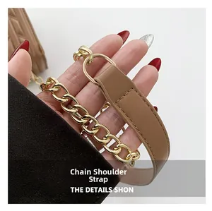 Detail of the golden chain shoulder strap with brown leather stitching and metal buckle