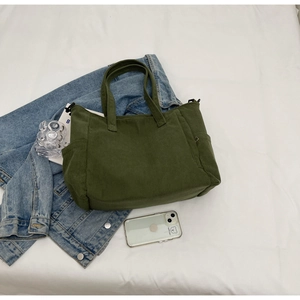 Detailed texture of green corduroy tote bag showing side pockets on white bedding