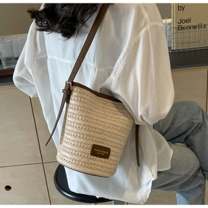 Detail shot of woven straw bucket bag with dark brown leather trim and thin strap