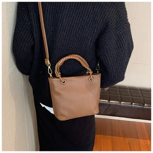 Side view of a brown pleated bucket bag worn as a shoulder bag on a black sweater