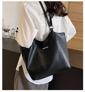 Close-up of black lychee grain tote bag with silver metal bar on white shirt