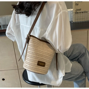 Detail of woven straw bucket bag with brown leather strap and logo on a seated model