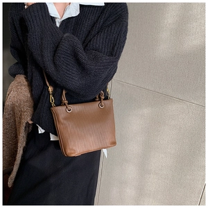 Close-up of brown pleated bucket bag with twisted handle and detachable strap on model