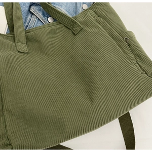 Close-up of dark green corduroy tote bag texture with metal eyelet detail and handle