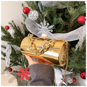 Detailed close-up of golden cylindrical mirror clutch bag with pearl clasp and chain