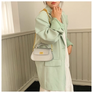 Detail of silver grey crossbody bag with gold twist lock and chain strap on green suit