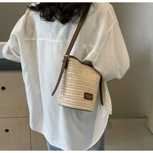 Detail shot of the woven straw bucket bag with dark brown leather straps and trim
