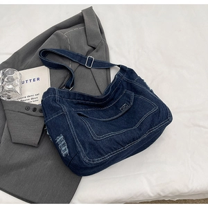 Dettaglio della borsa a tracolla in denim blu con bordi sfrangiati e fibbia in metallo argento