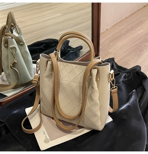 Close-up of quilted cream bucket bag with brown leather handles and gold metal hardware