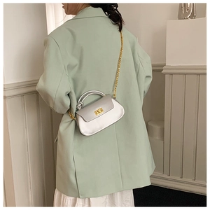 Silver square crossbody bag with gold chain strap shown on a model in a French style interior