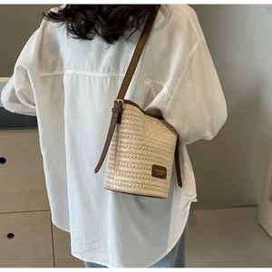 Close-up of woven straw bucket bag with brown leather trim and adjustable shoulder strap