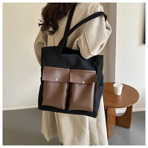 Detail view of large canvas tote bag featuring contrast brown leather front pockets and metal buttons