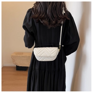 Detailed view of white V-quilted small crossbody bag with metal chain on black dress