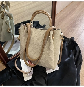 Detail of cream bucket bag with rhombus stitching and brown leather handles on black silk