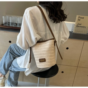 Detail of woven straw bucket bag with brown leather trim and adjustable shoulder strap