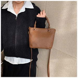 Brown pleated bucket bag with vertical texture and woven handle shown on model