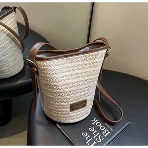 Detailed view of woven straw bucket bag with dark brown leather trim and metal hardware