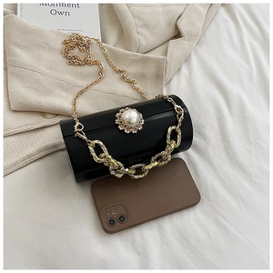 Detail of black acrylic cylinder clutch with pearl flower clasp and golden chain strap