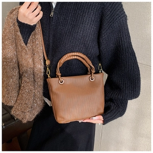 Close-up of brown pleated bucket bag featuring unique circular wrapped handle and hardware