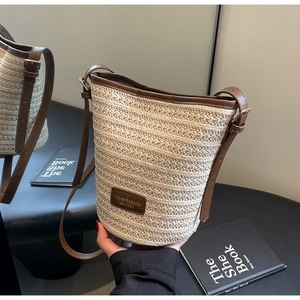 Close-up of beige woven straw texture and brown leather branding on bucket bag