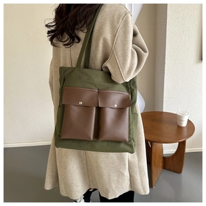Detail of dark green canvas tote featuring brown leather pockets and metal snap buttons