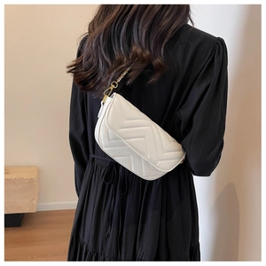 White quilted crossbody bag with gold chain strap shown on a black dress background