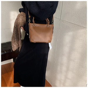Close-up of brown pleated bucket bag with twisted handle and gold hardware detail