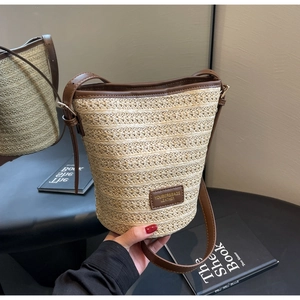 Detailed close-up of beige woven straw bucket bag with premium brown leather straps