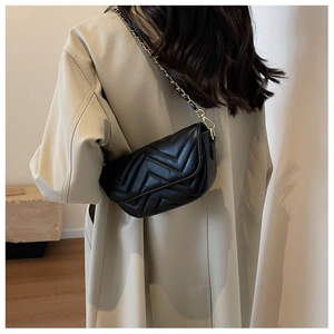 Detail view of a black quilted crossbody bag with a golden chain strap on a model