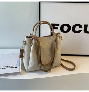 Detail of quilted beige bucket bag with brown leather handles and gold metal hardware
