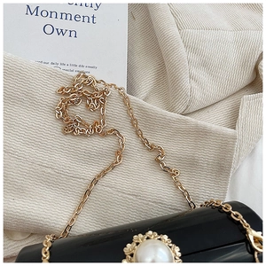 Close-up of black mirror acrylic cylinder bag featuring pearl clasp and gold chain