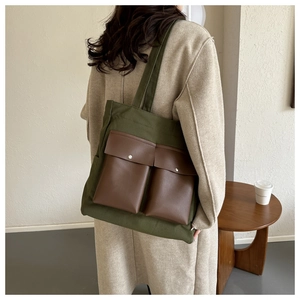 Detail view of the green canvas tote bag with brown leather pockets and metal buttons