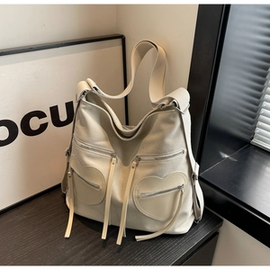 Close-up of beige canvas shoulder bag featuring heart-shaped zip pockets and long tassels