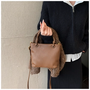 Detailed view of brown pleated bucket bag featuring round handles and a slim shoulder strap