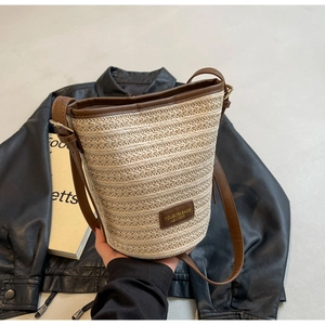 Detailed view of woven straw bucket bag with dark brown leather trim and brand label